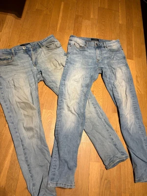 Två par ljusblå jeans  - Säljer två par ljusblå slim fit jeans med klassisk femficksdesign och snygga slitningar framtill. Båda paren har normal midja och raka ben. Perfekta för en avslappnad och trendig look. Materialet är bomullsdenim med lite stretch för extra komfort.