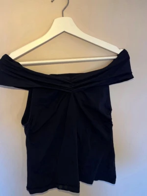 Mörkblå offshoulder topp - Snygg mörkblå offshoulder topp med draperad detalj framtill. Perfekt för dig som vill ha en stilren och trendig look. Toppens material känns mjukt och följsamt mot kroppen.