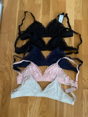 Spetsbhar i fyra färger - Fyra snygga bhar i spets, färgerna svart, mörkblå, ljusrosa och vit. Alla har justerbara axelband och klassisk hakknäppning bak. Triangelmodell utan vaddering, perfekt för dig som gillar komfort och stil. Materialet är mjukt och stretchigt med fina spetsdetaljer. Det finns ingen platta i bhn. En av de svarta är helt ny och aldrig använd men de andra är använda fåtal gånger.