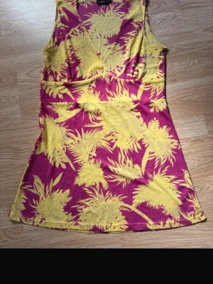 Somrig klänning/topp från Lindex – rosa/gul mönstrad, strl L - Färgstark och luftig klänning/topp som verkligen gör sommarlooken 🌸☀️  Härlig klänning/topp från Lindex i storlek L med ett livfullt rosa och gult mönster. Perfekt för varma dagar när du vill ha något både bekvämt och snyggt. Den har en smickrande passform med markerad midja och lätt utsvängd kjol.  Materialet är lite tunnare och lätt genomskinligt, vilket gör den extra sval – funkar perfekt med en underklänning eller shorts/topp under.  Detaljer: • Storlek: L • V-ringad • Ärmlös