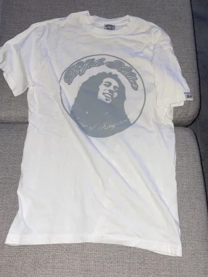 Vit Bob Marley t-shirt Commandante - Vit t-shirt från Commandante Clothing med stort tryck av Bob Marley och texten 'Buffalo Soldier' på framsidan. Baksidan har ett dekorativt kors och logotyp. Klassisk passform och rund hals.
