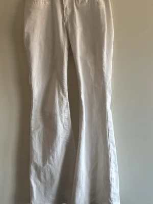 Vita utsvängda jeans och low rise - Säljer ett par vita jeans med utsvängda ben och klassisk femficksdesign. Jeansen har hög midja och raka sömmar, perfekta för en clean och fräsch look. Materialet är denim i bomull som känns mjukt och följsamt.