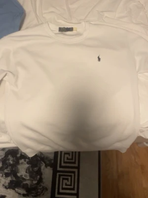 Vit sweatshirt från Polo Ralph Lauren - Klassisk vit sweatshirt från Polo Ralph Lauren med rund halsringning och den ikoniska lilla broderade loggan på bröstet. Tröjan har ribbade muddar vid ärmslut och nederkant. Perfekt för en clean och stilren look. Passar M och S