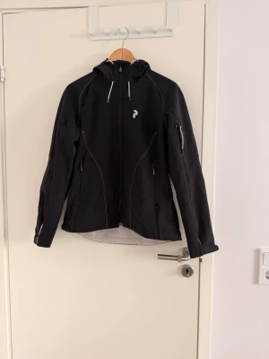 Peak Performance Softshell Jacket, Black  (fitted waist) - Size M - Svart vindjacka med huva från Peak Performance. Jackan i storlek M med fitted waist. 