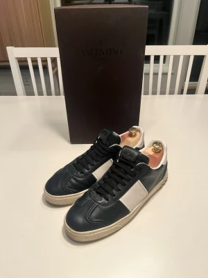  Valentino flycrews  - Stilrena sneakers från Valentino i svart och vitt läder med klassisk låg siluett. Skorna har svarta snören, vit sula och diskret Valentino-logga på tungan. Perfekta för dig som vill ha en clean och exklusiv look.