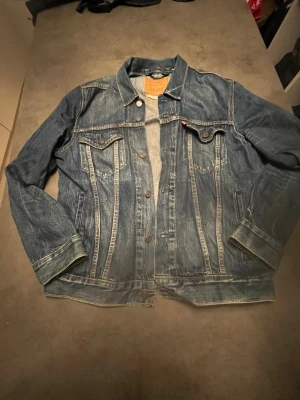 Levi's blå jeansjacka, storlek M - Klassisk blå jeansjacka från Levi's i modell Premium. Jackan har knäppning framtill, två bröstfickor med lock och knapp samt snygga kontrastsömmar. Perfekt oversized look och tidlös design med ikonisk Levi's-detalj på bröstet.