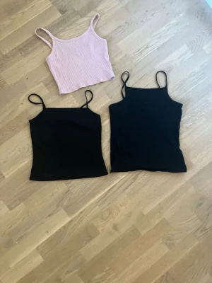 Tre linnen i svart och ljusrosa - Säljer tre linnen, två svarta och ett ljusrosa. De svarta har smala axelband och enkel design, medan det ljusrosa är ribbat och croppat med bredare axelband. Perfekta till sommaren och lätta att matcha med olika outfits.