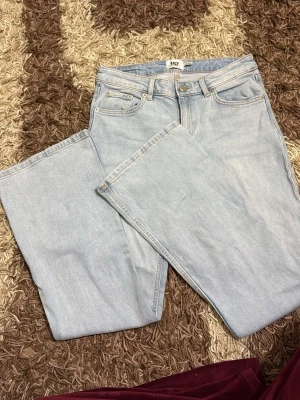 Ljusblå bootcut jeans - Säljer ett par ljusblå bootcut jeans med klassisk femficksdesign och hög midja. Jeansen har en snygg utsvängd passform nedtill och är tillverkade i mjukt denimtyg. Perfekta för dig som gillar retrovibbar och vill ha ett par bekväma jeans med stil.