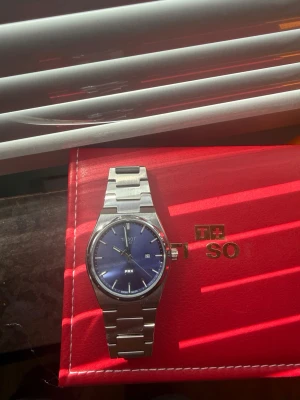 Tissot PRX blå - Snygg Tissot PRX klocka med blå urtavla och datumvisning. Klockan har ett stilrent armband i rostfritt stål och klassisk rund boett. Perfekt accessoar för dig som gillar tidlös design och schweizisk kvalitet. Kommer även extra länkar till 