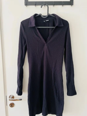 Mörkblå ribbad klänning  - Mörkblå ribbad klänning/ längre top med v-ringad krage. Är i stretchigt material som sitter skönt på kroppen. Passar stl S.