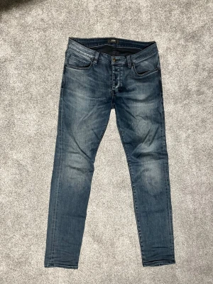 Blå slim fit jeans från Neuw - Snygga blå slim fit jeans från Neuw med klassisk femficksdesign och diskreta slitningar. Jeansen har en smal passform och är tillverkade i ett stretchigt denimtyg för extra komfort. Perfekta för en trendig och avslappnad stil.