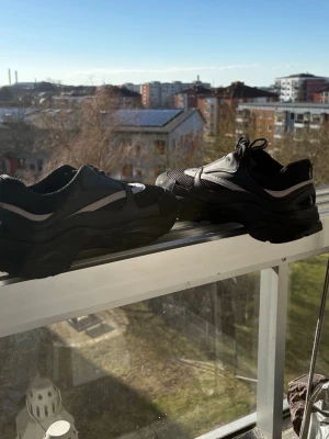 Chunky svarta sneakers med meshdetaljer - Säljer ett par chunky svarta sneakers med tjock sula och meshdetaljer. Skorna har svarta och grå inslag, snörning och en sportig vibe. Perfekta för dig som gillar streetwear och vill ha något som sticker ut lite extra.
