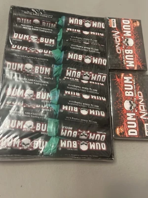 Dum Bum fyrverkeripjäser - Säljer ett paket Dum Bum fyrverkeripjäser och Dum Bum Nano. Svarta fyrverkerier med vit och röd text samt dödskallemotiv. Förpackningarna är rektangulära och har gröna stubiner. Perfekt för dig som gillar pyroteknik och vill ha något extra till firandet.
