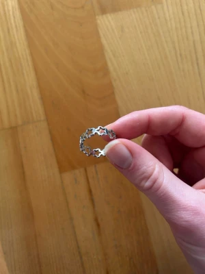Söt silverring med stjärnor - Unik ring i silverfärgad metall med ett mönster av sammanlänkade stjärnor runt hela ringen. Perfekt för dig som gillar detaljer med lite extra personlighet och vill ha något som sticker ut. Enkel men ändå lekfull design som passar till många stilar.