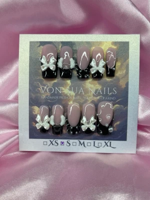 BbyNoir (S);Medium Square - Unika handgjorda press-on naglar i svart och nude med 3D vita rosetter och pärldetaljer. Naglarna har en cool, square form och dekoreras med vita vingar 🪽 för extra attityd. Perfekt för dig som vill sticka ut med en edgy och söt look.S: 15 mm, 11,5 mm, 12 mm, 11 mm, 9 mm 