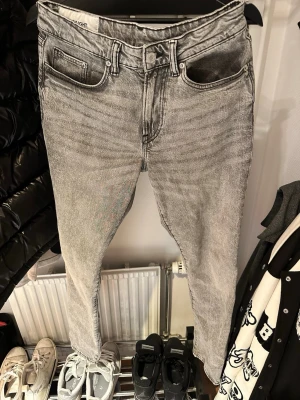 Grå tvättade jeans från HM - Säljer ett par grå tvättade jeans från Weekday med klassisk femficksmodell och raka ben. Jeansen har hög midja och är tillverkade i ett mjukt denimtyg. Perfekta för en avslappnad och trendig look.