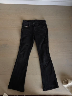 Svarta bootcut jeans från Diesel - Snygga svarta jeans från Diesel med bootcut-modell och klassisk femficksdesign. Jeansen har en liten logga på myntfickan och är tillverkade i ett starkt denimtyg med lätt tvättad look. Perfekta för en trendig och avslappnad stil som kan användas mycket! 