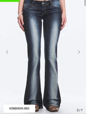 Blå bootcut jeans med slitningar - Snygga blå bootcut jeans med markerade slitningar och ljusare tvätt längs benen. Klassisk femficksmodell med låg midja och dragkedja. Perfekta för en avslappnad och trendig look. Storlek 26/32, passar mig som är 166cm och brukar har xs.