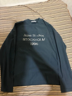 Acne studios longsleeve - Snygg blå långärmad t-shirt från Acne Studios med trycket 'Acne Studios STOCKHOLM 1996' i vitt framtill. Klassisk rund hals och relaxed fit. Perfekt för dig som gillar stilrena plagg med en urban touch.