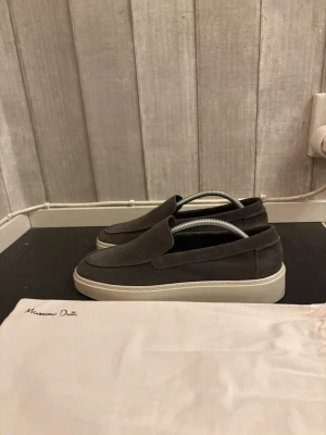 Gråa loafers från Massimo Dutti - Snygga loafers i grå mocka från Massimo Dutti med vit tjock sula. Skorna har en stilren och minimalistisk design utan snörning, perfekt för en clean och modern look. Kommer med dustbag. Ny pris 1300 knappt använda endast lite lätt ett fåtal gånger, vid frågor skriv 