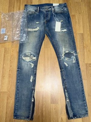 Blå slitna jeans med dragkedjor från (Mnml)  - Säljer ett par blå jeans med dragkedjor vid bensluten. Jeansen har en tvättad look och raka ben. Perfekta för dig som gillar en edgy och trendig stil. Jeansen är från MNML 