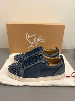 Blåa Christian Louboutin sneakers - Snygga blåa sneakers från Christian Louboutin i mocka med matchande blå snören och coola nitar på tån. Skorna har vit sula och en låg profil som ger en clean look. Perfekta för dig som vill sticka ut med exklusiva detaljer.