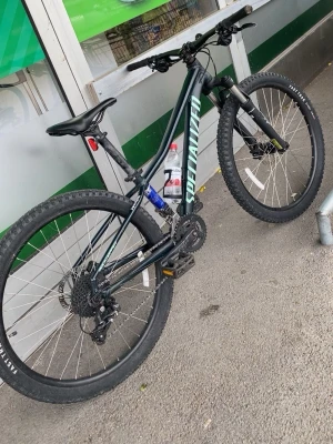 Specialized svart mountainbike - Säljer en svart mountainbike från Specialized med gröna detaljer. Cykeln har grova däck, framdämpare från RockShox och sportig ram. Utrustad med vattenflaskhållare och Shimano-växlar. Perfekt för dig som gillar att cykla i terräng och skog.