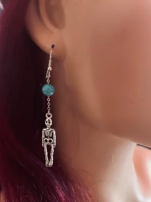By prisförslag- 1 st Skelettörhänge med turkos pärla - Unikt örhänge med ett silverfärgat skelett i metall och en turkos pärla ovanför. Hängande modell med cool och edgy vibe, perfekt för dig som gillar statement-smycken och vill sticka ut. Passar till dig som gillar alternativa accessoarer.
