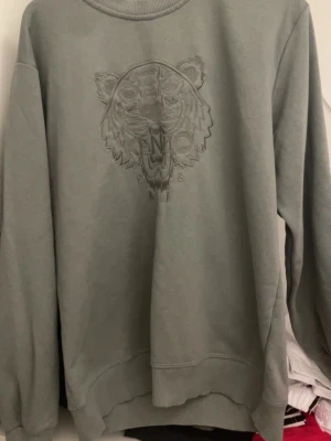 Grön sweatshirt från Kenzo med tiger - Säljer en grå sweatshirt från Kenzo med det ikoniska tigerhuvudet broderat på bröstet. Storlek XL men skulle säga att den passar L
