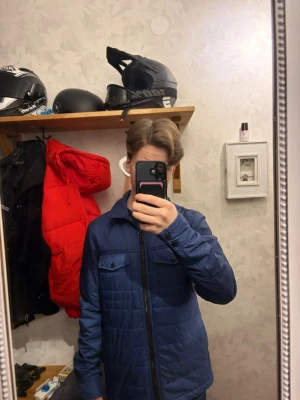 Blå quiltad cardiganjacka - Snygg blå quiltad cardiganjacka från J.Lindeberg  med dragkedja framtill och två bröstfickor med knapplock. Jackan har en rak passform och långa ärmar, perfekt för lager på lager under kyligare dagar. Enkel och stilren design som passar till det mesta.        Den ena dragkedjan på fickan  är sönder men går säkert att fixa. Priset är inte hugget i sten, skriv om ni undrar något. Original pris~3500