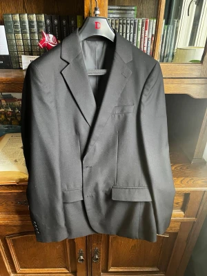 Svart kavaj Dressmann storlek 48 - Svart kavaj från Dressman. Storlek 48 regular, slim fit. Använd ett fåtal gånger och i mycket bra skick. Säljer för att den är för stor för mig. Om du undrar något är det bara att skriva 🤩