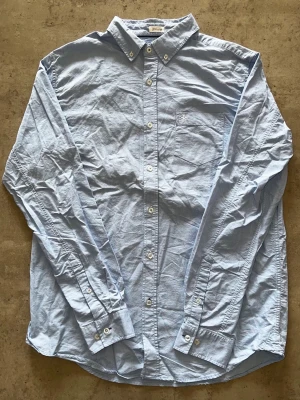 Ljusblå skjorta från Lager157 - L - Klassisk ljusblå skjorta från Lager157 med button-down krage och bröstficka. Skjortan har vita knappar och lång ärm, perfekt för en clean och stilren look. Tillverkad i bomull för skön känsla och enkel matchning.