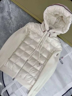 Vit pufferjacka från Moncler - Snygg vit pufferjacka från Moncler med quiltad front och stickade ärmar. Jackan har en stor huva med dragsko och diskreta röda och blå detaljer vid huvkanten. Dragkedja framtill och Moncler-logga på ärmen. Perfekt för kalla vinterdagar.
