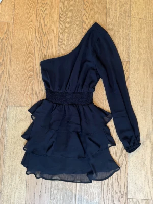 Oneshoulder volangklänning  - Säljer en svart oneshoulder klänning från Gina Tricot med lång ärm och volangkjol. Supersnygg klänning men har tyvärr blivit för liten. Använd ett fåtal gånger❣️
