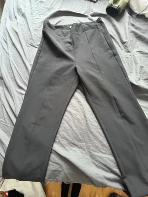 Svarta raka kostymbyxor - Säljer ett par svarta kostymbyxor med rak passform och pressveck. Byxorna har hög midja och stängs med dragkedja fram. Materialet känns slätt och något stretchigt, perfekt för en clean och stilren look.