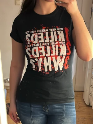 Svart t-shirt med tryck - Cool svart t-shirt med stort tryck i vitt och rött framtill. Texten lyder 'How many walkers have you killed? How many people have you killed? Why?' och har en blodstänksdesign. Perfekt för dig som gillar zombieserier och vill sticka ut.