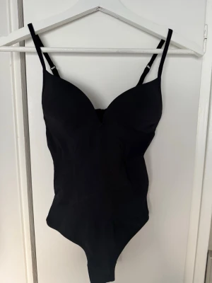 Svart body med justerbara band - Snygg svart body med vadderade kupor och justerbara axelband. Klassisk, enkel design utan synliga detaljer eller mönster. Tillverkad i stretchigt material som formar sig efter kroppen. Perfekt att styla under skjorta eller kavaj.