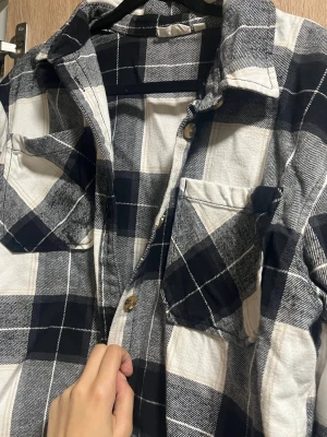 Svartvit rutig kofta  med fickor från Kappahl  - Säljer en svartvit rutig Kofta  i mjuk bomull från Kappahl . koftan har två bröstfickor med lock, klassisk krage och knäppning framtill. Perfekt för en avslappnad och trendig look. Passar lika bra öppen som stängd. Använt någon gång bara