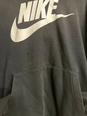 Svart Nike hoodie med stor logga - Säljer en svart hoodie från Nike med stor vit logga och swoosh på bröstet. Klassisk känguruficka framtill och huva. Tillverkad i mjukt bomullsmaterial som är skönt att ha på sig. Perfekt för dig som gillar streetwear och sportig stil.