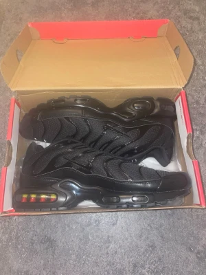 Nike Air Max Plus svarta sneakers - Nike Air Max Plus sneakers i helsvart med mesh och syntetpaneler, ikoniska vågmönster och synlig Air-enhet i sulan med färgdetaljer. Klassisk Nike-logga på plös och häl. Snygg och sportig design som sticker ut. Oanvänd utan kvitto