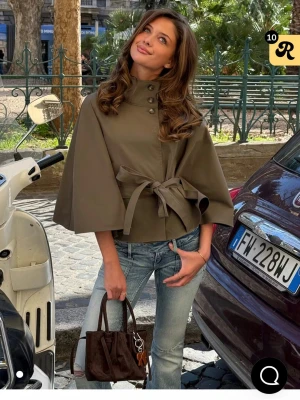 Olivgrön cape-kappa med knytband - Stilren olivgrön ponsho jacka med hög krage. Superfin aldrig använd!