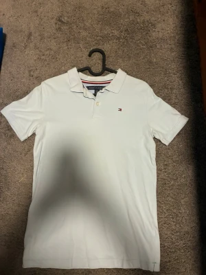 Ljusblå Tommy Hilfiger Piké - Unik ljusblå pikétröja från Tommy Hilfiger med liten logga på bröstet. Tröjan har krage, knappar vid halsen och korta ärmar. Perfekt till en clean och stilren look.