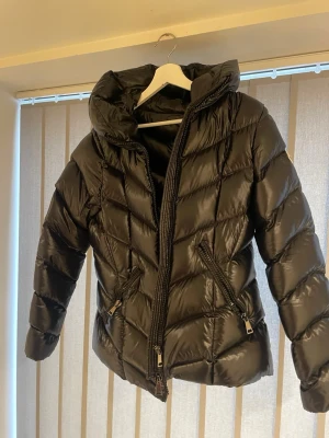 Svart moncler jacka med huva - Säljer en svart pufferjacka med stor huva och dragkedja framtill. Jackan har två snedställda fickor med dragkedja och quiltad design i ett glansigt material. Perfekt för kalla dagar och riktigt snygg till streetwear-stilen. Jackan är xxl men passar mycket bättre mindre storlekar, tjejen sista bilden är 167 och använder xs normalt sätt för referens