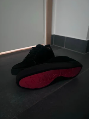 Svarta Christian Louboutin sneakers - Snygga svarta sneakers från Christian Louboutin med klassisk röd sula och låg profil. Skorna har en stilren design med svarta skosnören och diskret logga på sidan. Perfekta för dig som vill ha något exklusivt och trendigt i garderoben.
