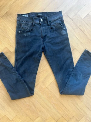 Svarta  jeans från Replay - Säljer ett par svarta slim jeans från Replay med klassisk femficksdesign och knappgylf. Jeansen har en snygg tvättad look och är tillverkade i stretchigt material för skön passform. Perfekta till en avslappnad stil.27/32