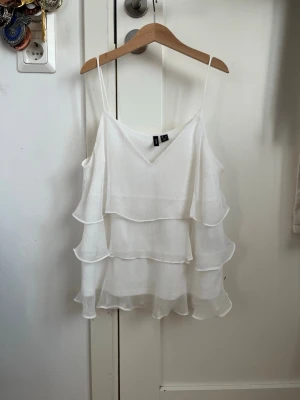 Vit volangig linnetopp med smala band - Säljer en superfin vit linnetopp med tunna axelband och flera lager volanger. Toppen har v-ringning och är perfekt för varma dagar. Luftigt material som ger en flowy känsla och passar snyggt till både jeans och kjol.