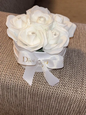 Evighetsrosor i blombox med vita Glitter rosor - Säljer en rund dekorativ blombox med vita konstgjorda rosor och glittriga detaljer. Boxen är prydd med ett vitt band med guldfärgad rosettband och en söt rosett framtill. Perfekt som inredningsdetalj eller present.