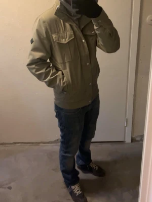 J.Lindeberg filedjacket - Snygg jacka från J.Lindeberg med huva och tryckknappar framtill. Jackan har två bröstfickor med lock och två sidofickor. Perfekt för dig som vill ha en stilren och funktionell jacka till vardags.