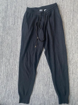 Svarta mjukisbyxor Markus Lupfer - Snygga svarta mjukisbyxor från Markus Lupfer med dragsko i midjan och ribbade muddar vid bensluten. Tillverkade i ett mjukt och stretchigt material som känns riktigt skönt mot huden. Perfekta för chill dagar eller när du vill ha en avslappnad look.Svarta och silvriga joggingbyxor i merinoull strl S fr Markus Lupfer  Sparsamt använda och i fint begagnat skick   Mått Midjan: ca 34 cm Längd från grenen och ner: ca 69 cm  70% merinoull och 30% metalltråd   Kommer från ett djur och rökfritt hem