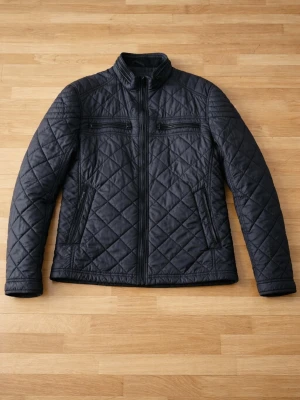 Svart quiltad jacka från Tom Tailor - Snygg svart quiltad jacka från Tom Tailor med dragkedja framtill och ståkrage. Jackan har två bröstfickor med dragkedja och två sidofickor. Perfekt för dig som gillar en stilren och modern look. Storlek L men sitter som M